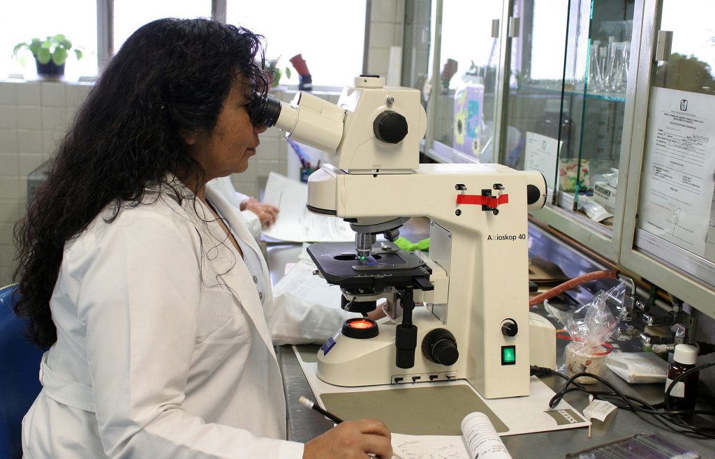Une femme en blouse blanche observe au microscope dans un laboratoire.