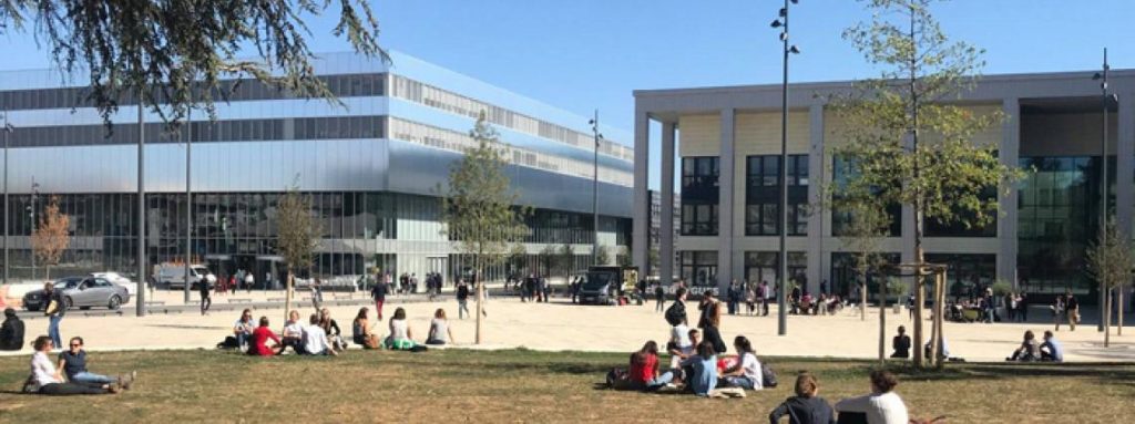 Plusieurs étudiants sur un coin d'herbe devant le bâtiment Bouygues et Eiffel de l'école CentraleSupélec.