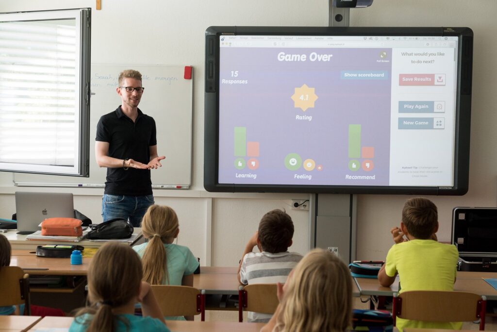 Un homme en face d'enfants dans une classe, avec un tableau numérique.
