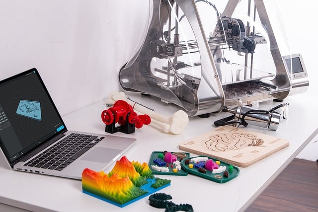 Un ordinateur portable, une imprimante 3D et des objets imprimés en 3D sont posés sur une table.