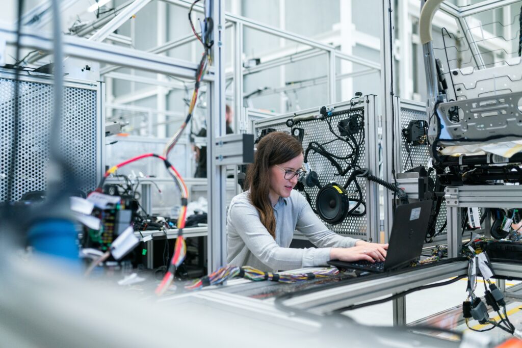 Une femme est devant son ordinateur portable dans une salle avec des câbles et des instruments informatiques.