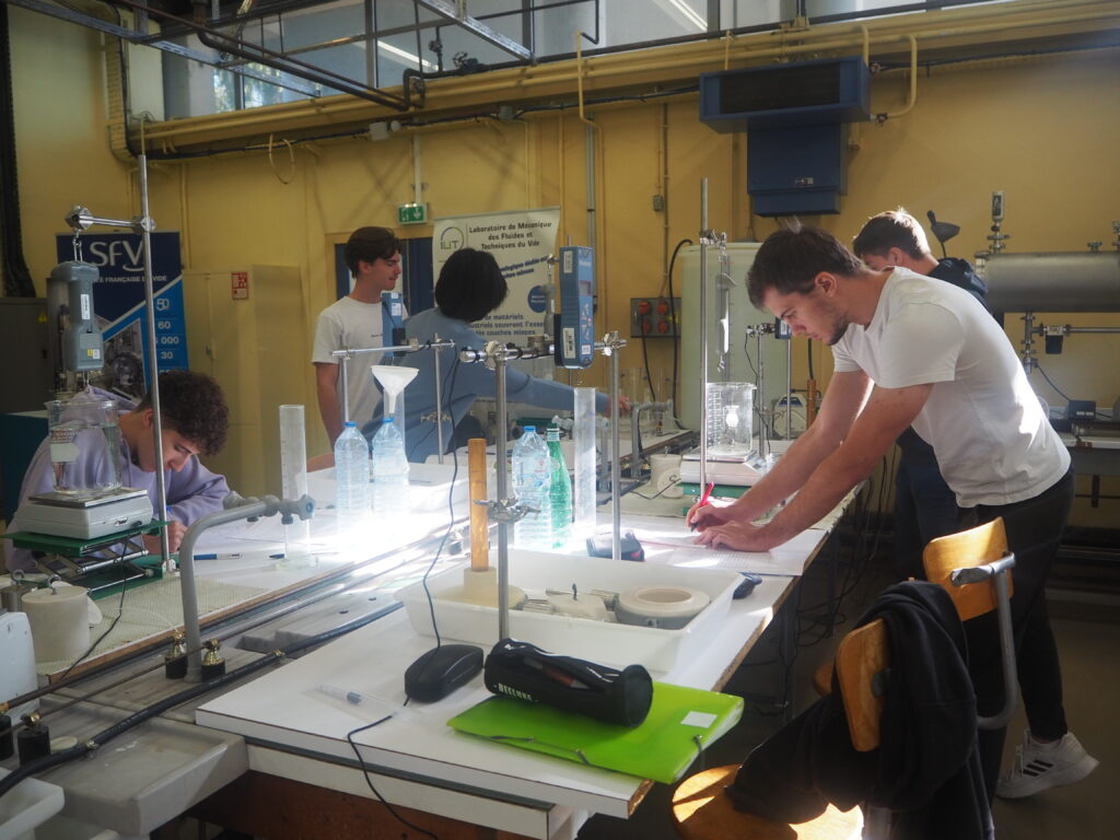 Cinq étudiants manipulent dans un laboratoire et prennent des notes sur leurs cahiers.
