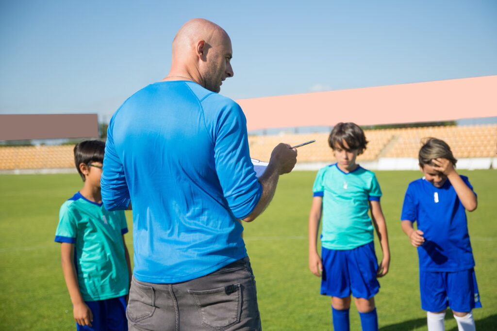 Un professeur de sport parle à trois enfants dans un stade de football.