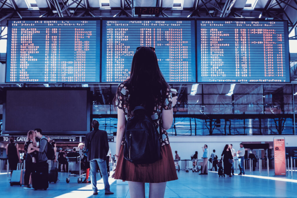 Une femme se tient devant l'écran d'affichage des vols dans un aéroport.