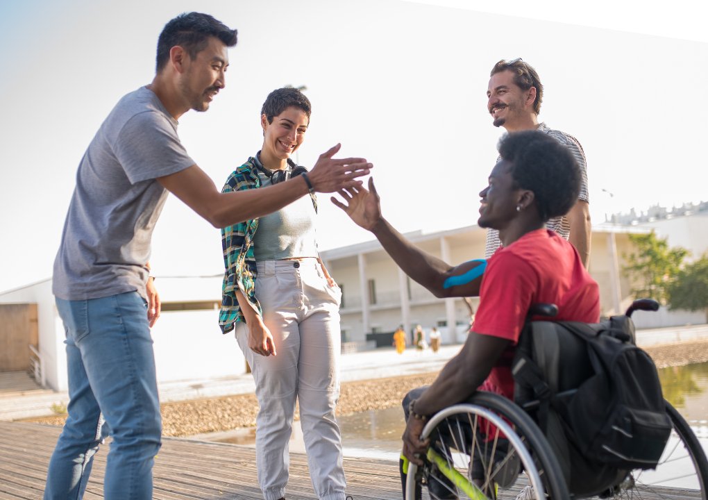 Quatre étudiants se parlent, l'un est en fauteuil roulant et tape dans la main de son ami.