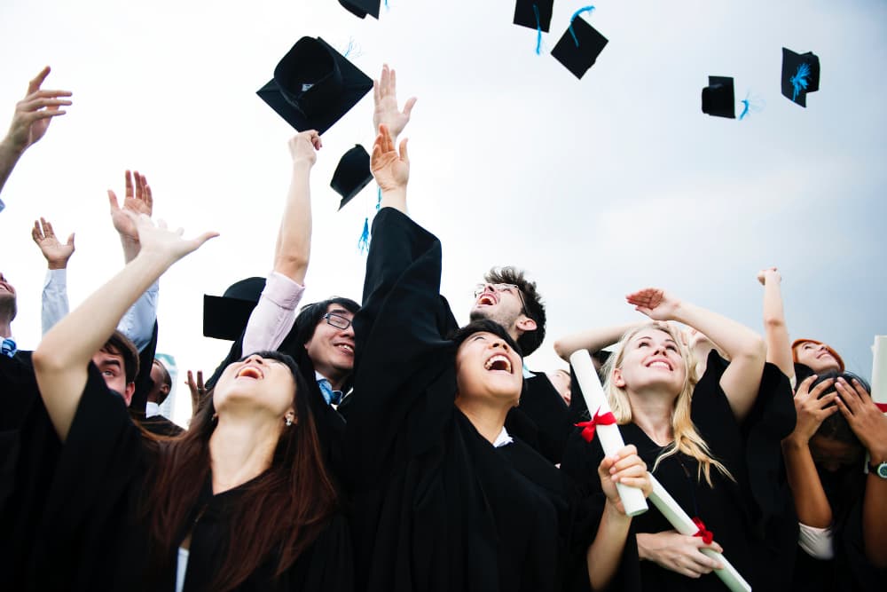 Plus de dix étudiants en toges noires, jettent leur toque en l'air.