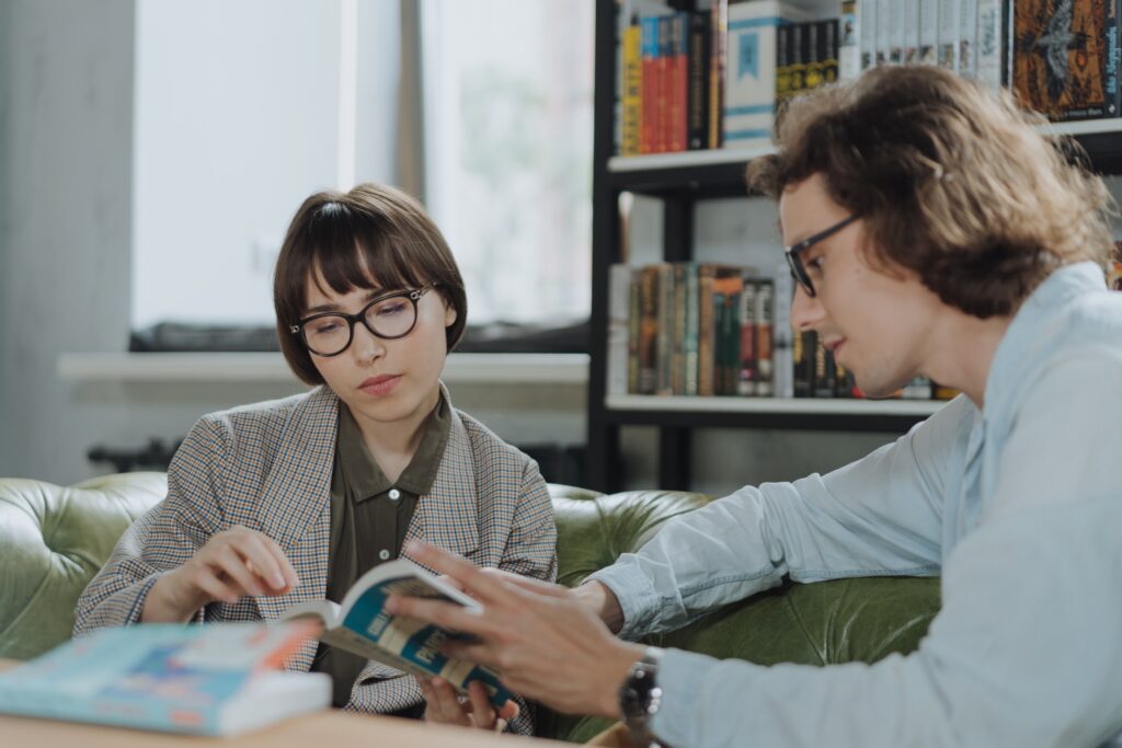 Une femme et un homme sont assis et discutent à propos d'un livre dans une bibliothèque.