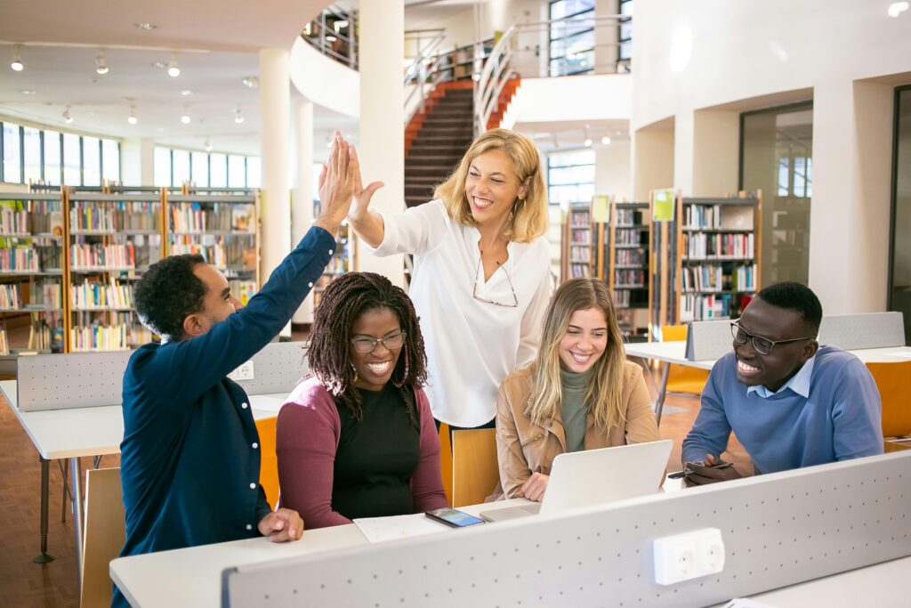 Quatre étudiants travaillent dans une bibliothèque, l'un deux tape dans la main d'une accompagnatrice.
