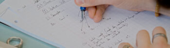 Une personne écrit sur une feuille de cours des formules algébriques avec u stylo plume.