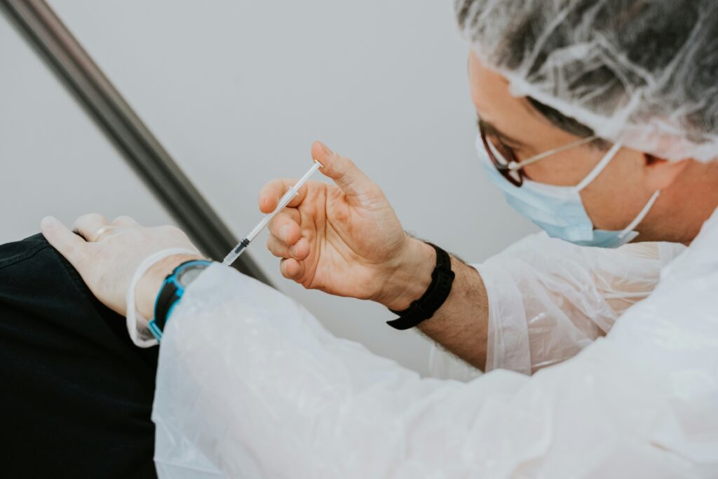 Une dame en blouse avec un masque et un gant, applique un vaccin à une autre personne, pour représenter la santé publique.