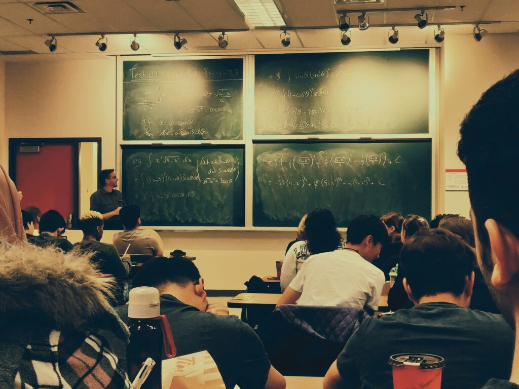 Un professeur de mathématiques donne cours dans une salle de classe devant des étudiants.